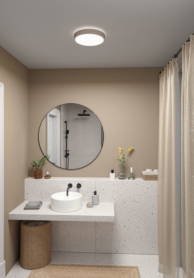 Round ceiling light with beige fabric edge illuminating modern bathroom with terrazzo sink.