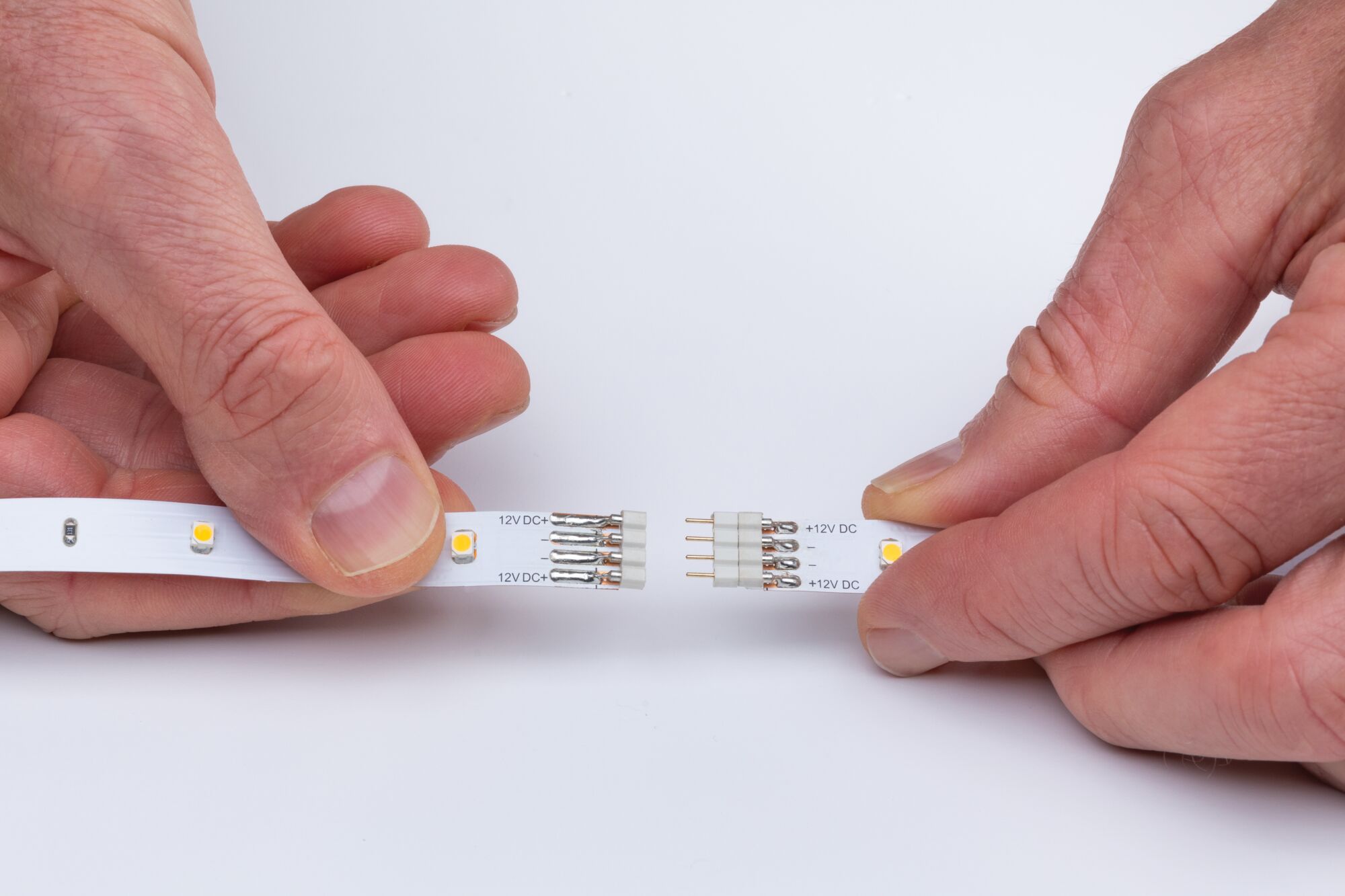 Hands connecting two white LED strips with 12V DC connectors for flexible lighting setups.