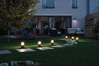 Moderne Gartenwegbeleuchtung mit schwarzen LED-Leuchten auf grünem Rasen vor Terrasse mit Sitzmöbeln