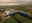 Luchtfoto van groot blauw industrieel gebouw omgeven door groene velden en parkeerplaatsen bij zonsopgang