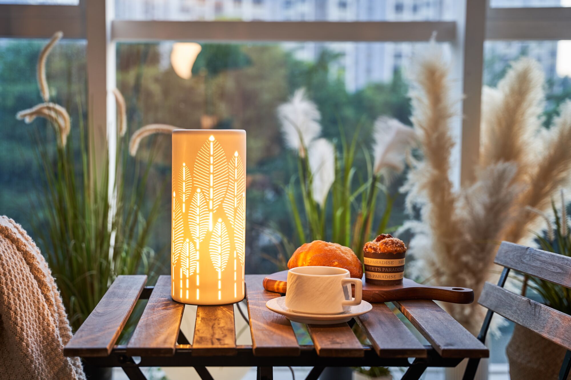 Lampe de table en céramique à motif de feuilles éclairée chaleureusement sur table en bois avec café et pâtisseries
