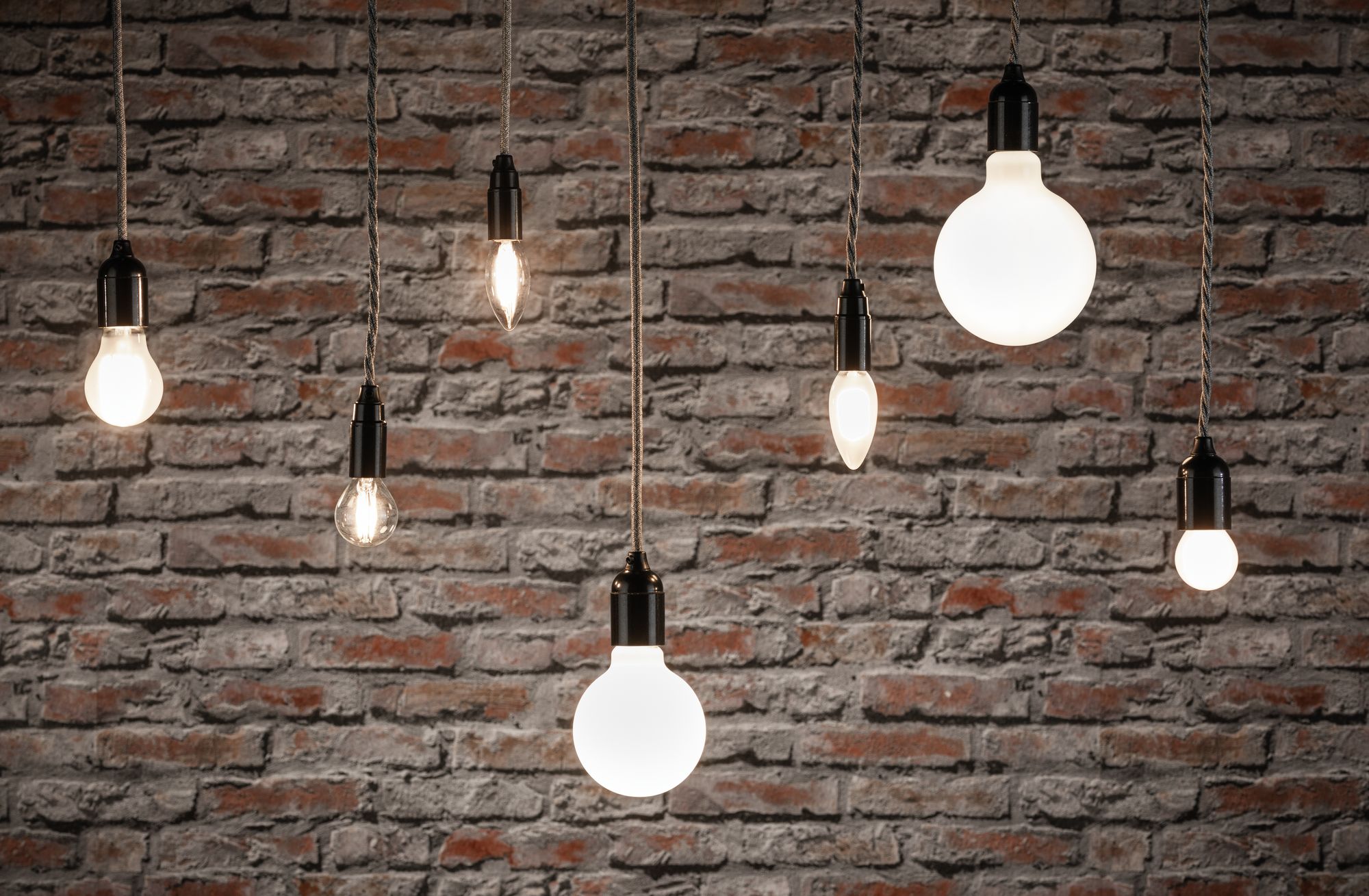 Various filament light bulbs with black sockets hanging in front of red brick wall, lighting and lamps.