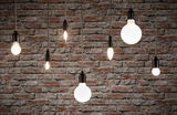 Diverse filamentlampen met zwarte fittingen hangend voor een rode bakstenen muur, verlichting en lampen.