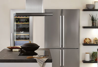 Modern kitchen featuring stainless steel fridge, wine cooler, and island with black cooktop and hood.