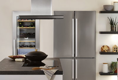 Modern kitchen featuring stainless steel fridge, wine cooler, and island with black cooktop and hood.
