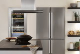 Moderne Küche mit Edelstahl-Kühlschrank, Weinkühler und Kochinsel mit schwarzem Kochfeld und Dunstabzug.