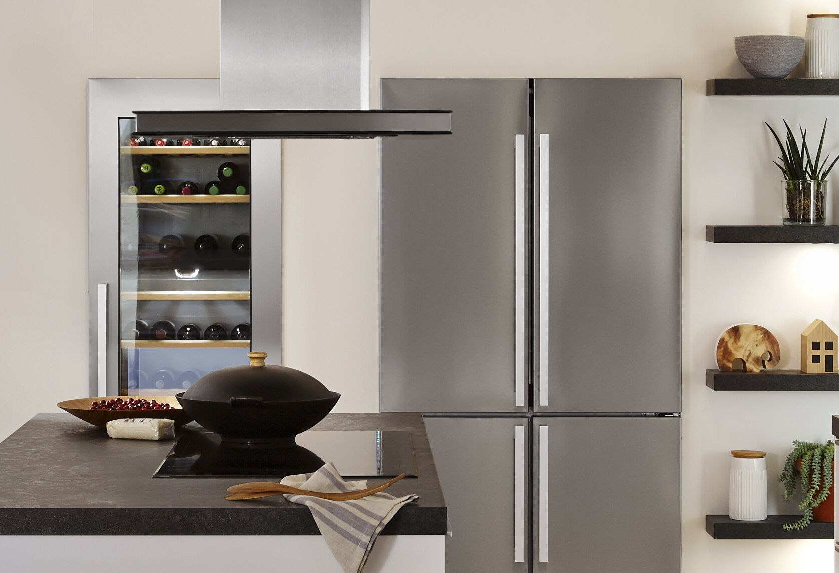 Cuisine moderne avec réfrigérateur en acier inoxydable, cave à vin et îlot avec plaque de cuisson noire et hotte.