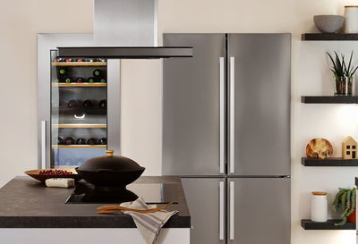 Cuisine moderne avec réfrigérateur en acier inoxydable, cave à vin et îlot avec plaque de cuisson noire et hotte.