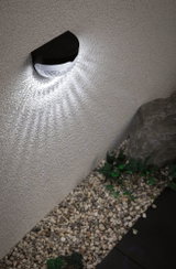 Applique murale solaire noire avec LED blanche sur mur extérieur au-dessus de gravier et plantes pour éclairage jardin