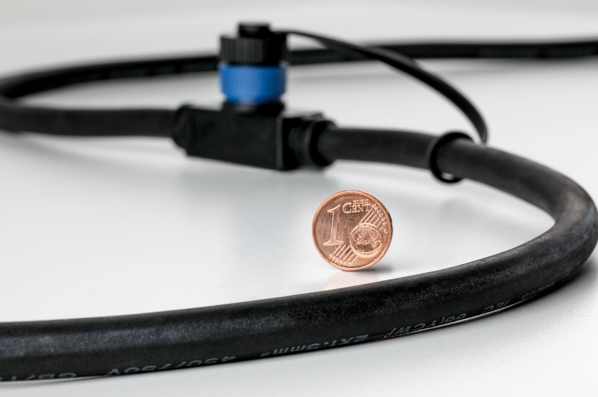 Zwarte kabel met blauwe connector en 1-cent munt voor maatvergelijking op witte achtergrond