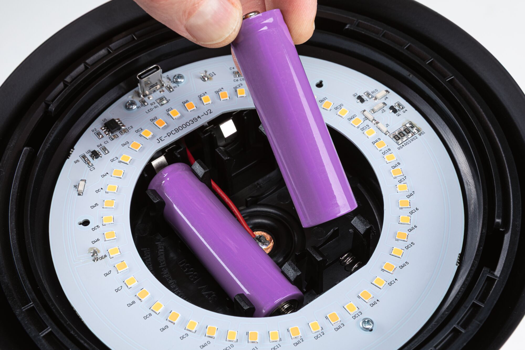 Hand legt violette 18650 Lithium-Ionen-Akku in LED-Leuchtenmodul mit weißen LEDs und schwarzem Gehäuse