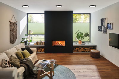 Salon moderne avec cheminée noire, sol en bois, murs blancs et plafonniers ronds.