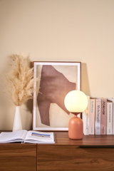 Modern table lamp with round opal white glass and terracotta ceramic base on wooden sideboard.