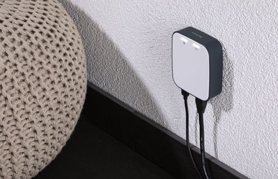 Adaptateur mural compact blanc et noir avec voyants LED sur mur texturé près d’un coussin en tricot beige