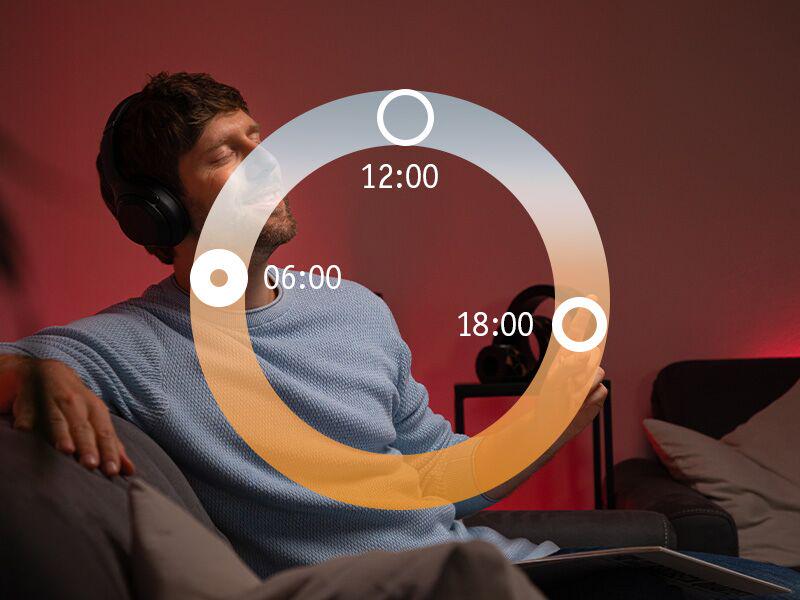 Mann entspannt auf Sofa mit Kopfhörern in warmrotem Licht, HCL-Lichtzyklus für Abendstimmung.