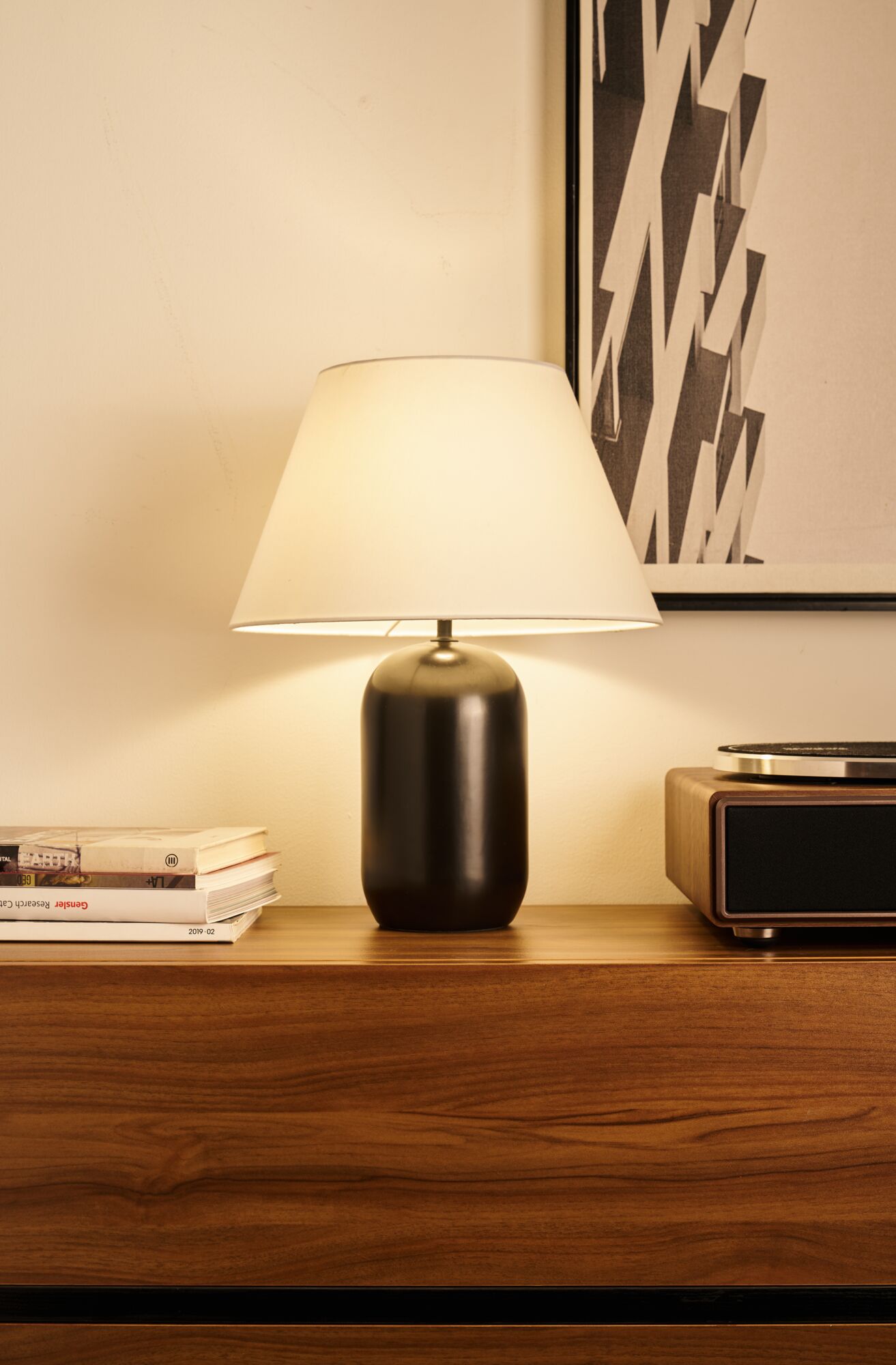 Moderne Tischlampe mit schwarzem Metallfuß und weißem Stoffschirm auf Holzkommode im Wohnzimmer