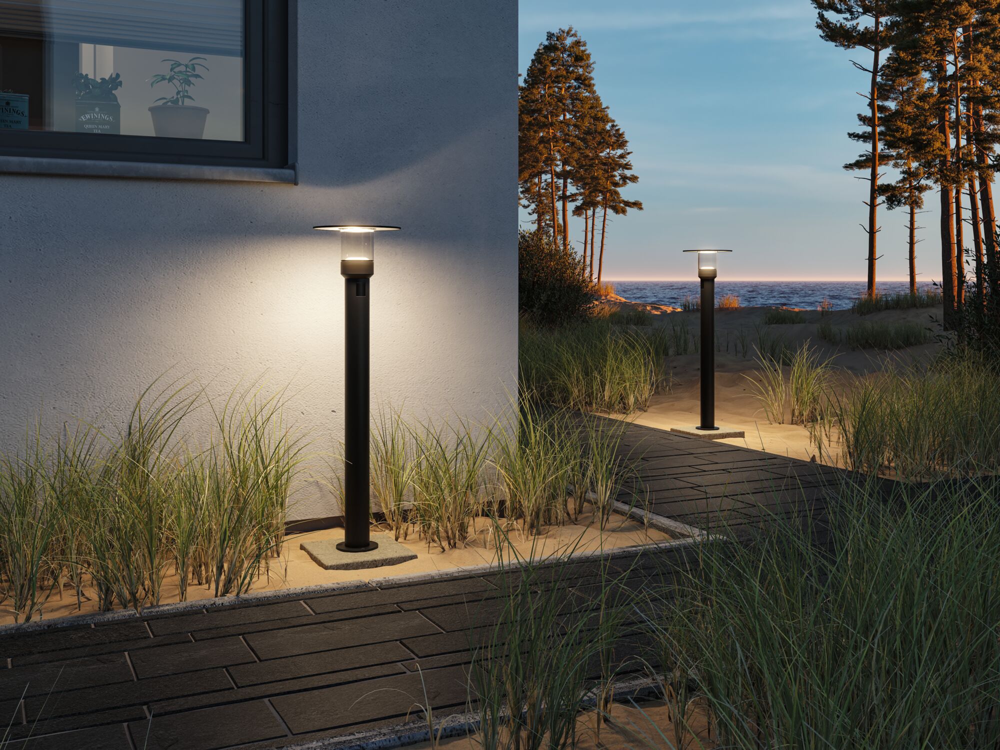 Modern black metal outdoor lamp with warm white light by house and path in sandy area.