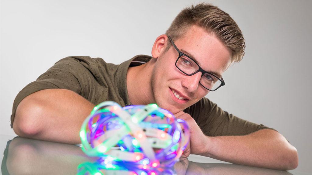 Junger Mann mit Brille betrachtet bunte LED-Lichtstreifen auf reflektierender Oberfläche, E-Commerce Kontext