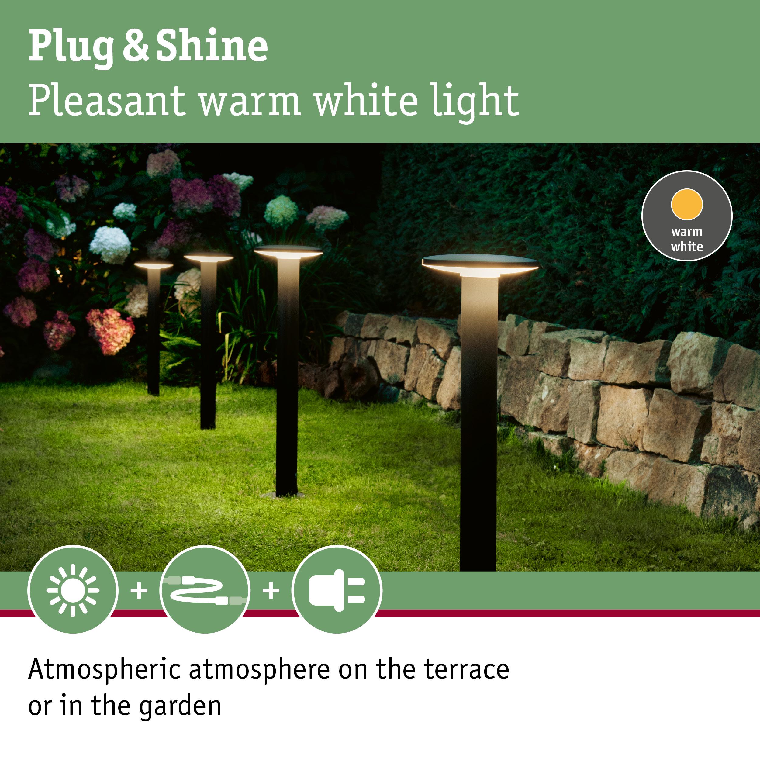 Black outdoor garden lights with warm white glow on grass near stone wall for terrace lighting