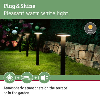 Black outdoor garden lights with warm white glow on grass near stone wall for terrace lighting