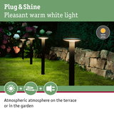 Black outdoor garden lights with warm white glow on grass near stone wall for terrace lighting