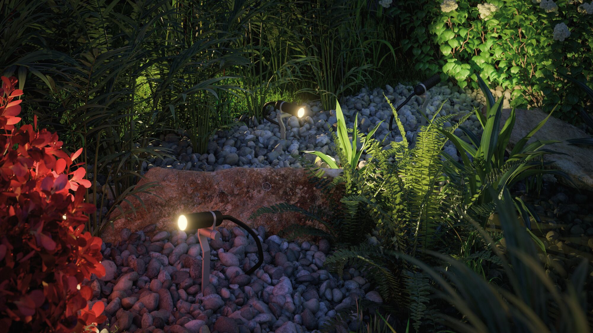 Drei schwarze LED-Gartenstrahler auf Kies mit grünen Pflanzen und rotem Busch für Außenbeleuchtung.
