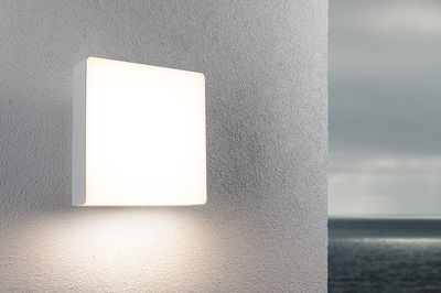 Square white plastic wall light with warm white illumination for outdoor use.
