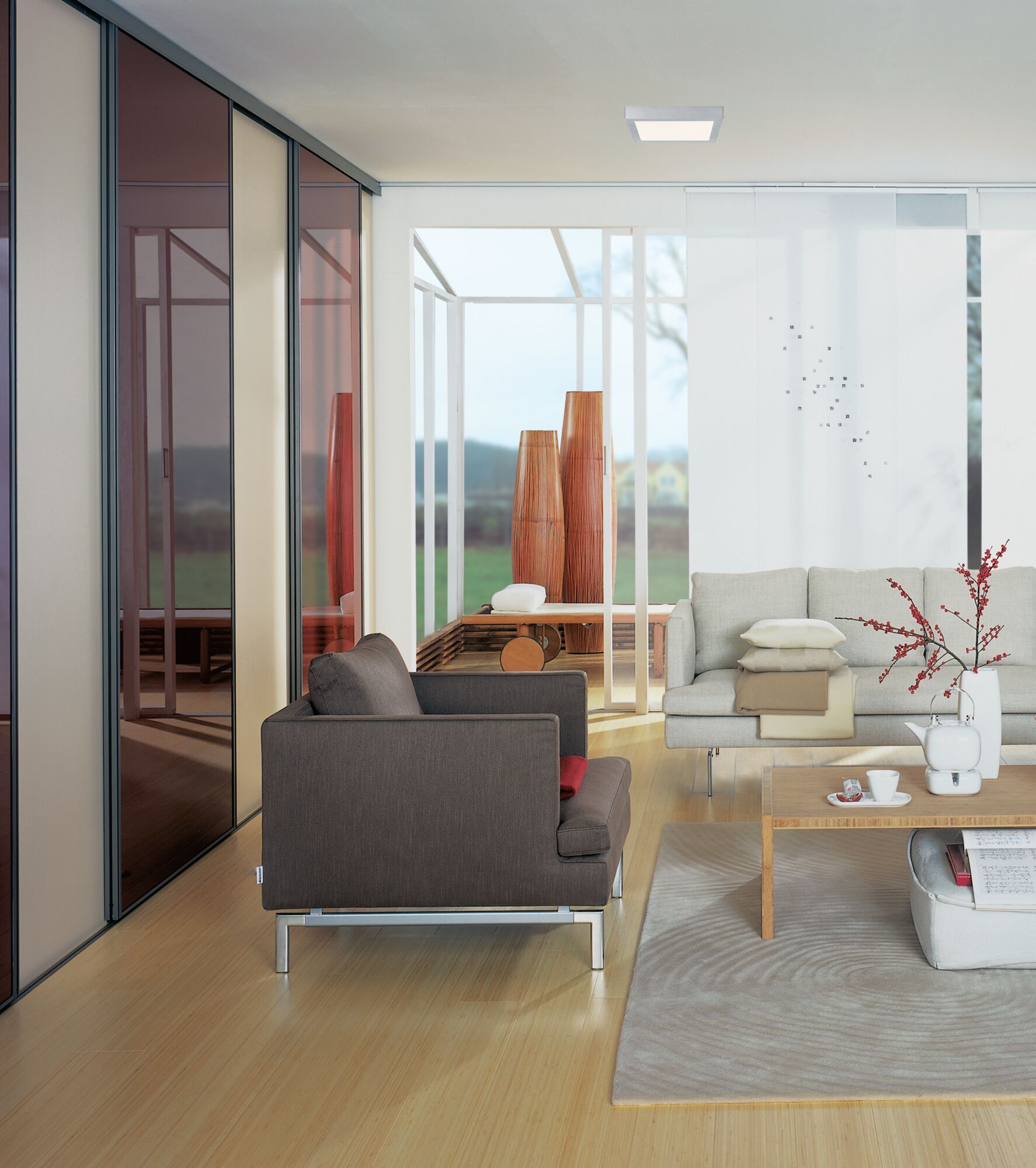 Modernes Wohnzimmer mit braunem Stoffsessel, hellem Sofa und quadratischer Deckenleuchte in Weiß.