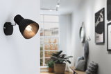 Schwarze Wandlampe aus Metall mit verstellbarem Leuchtkopf in modernem Wohnzimmer mit Fenster.