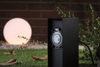 Prise extérieure noire avec minuterie intégrée dans un jardin avec lumière sphérique éclairée.