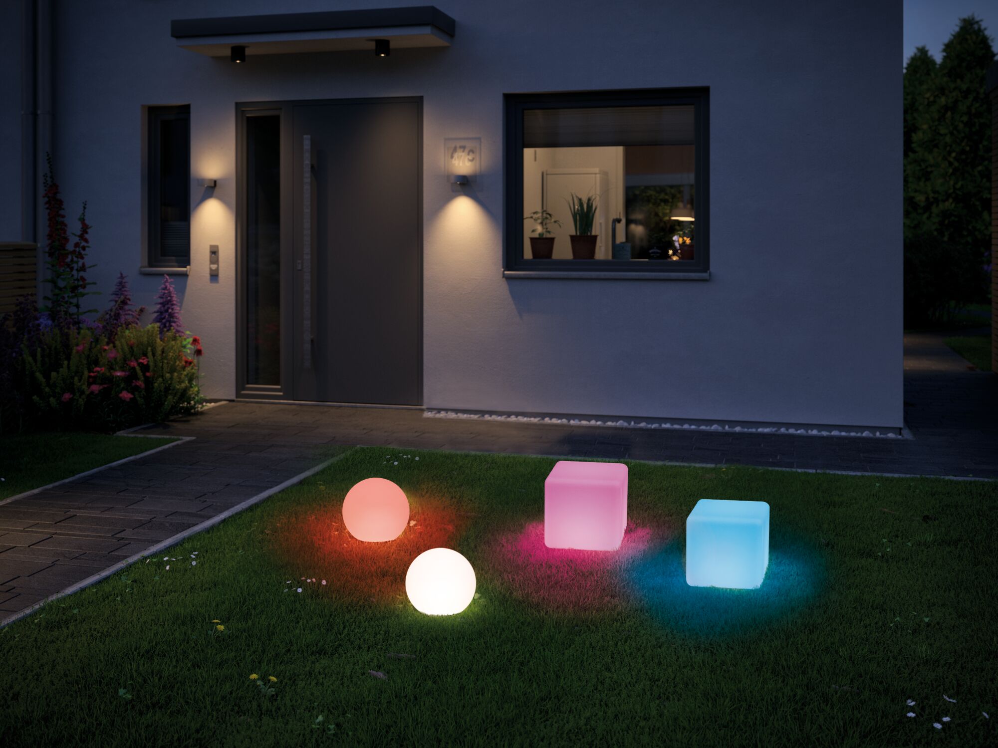 Colorful LED garden lights in sphere and cube shapes on lawn in front of modern house entrance at night