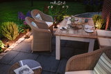 Terrasse confortable avec mobilier en rotin et table de jardin en bois, éclairage extérieur d'ambiance.
