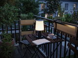 Modern white plastic table lamp on balcony with wooden chair and plants, ambient outdoor lighting