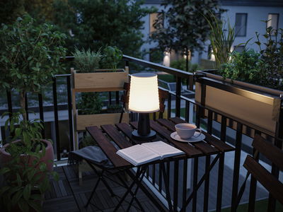 Moderne weiße Tischleuchte aus Kunststoff auf Balkon mit Holzstuhl und Pflanzen, stimmungsvolle Außenbeleuchtung