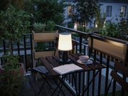Modern white plastic table lamp on balcony with wooden chair and plants, ambient outdoor lighting