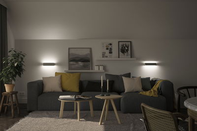 Modern living room with grey sofa, yellow and beige cushions, wooden tables and wall lights for ambient lighting