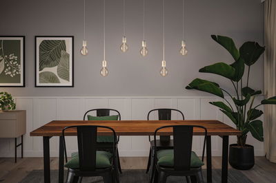 Modern dining area with wooden table, black metal chairs, and seven hanging LED light bulbs.