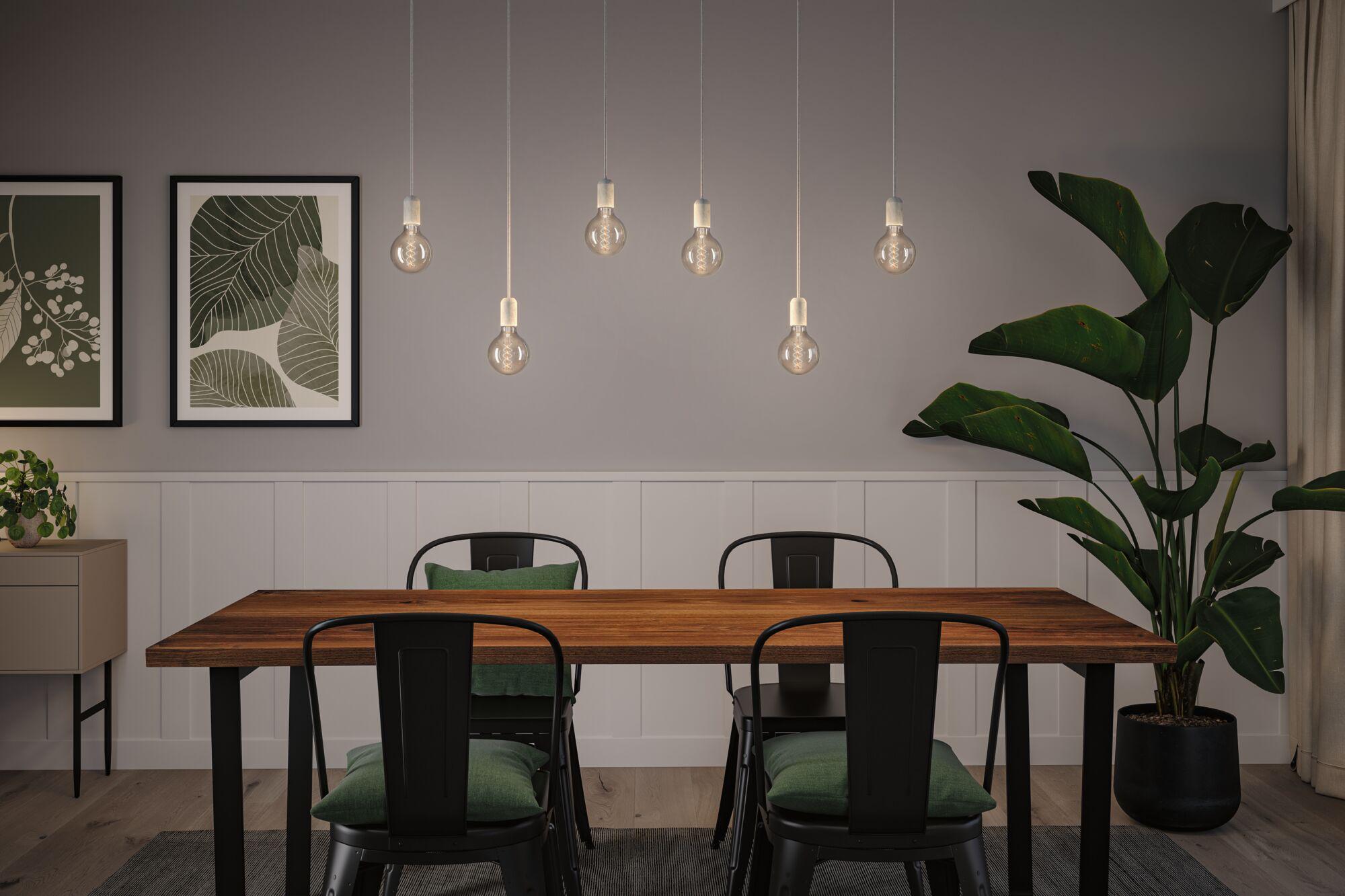 Modern dining area with wooden table, black metal chairs, and seven hanging LED light bulbs.