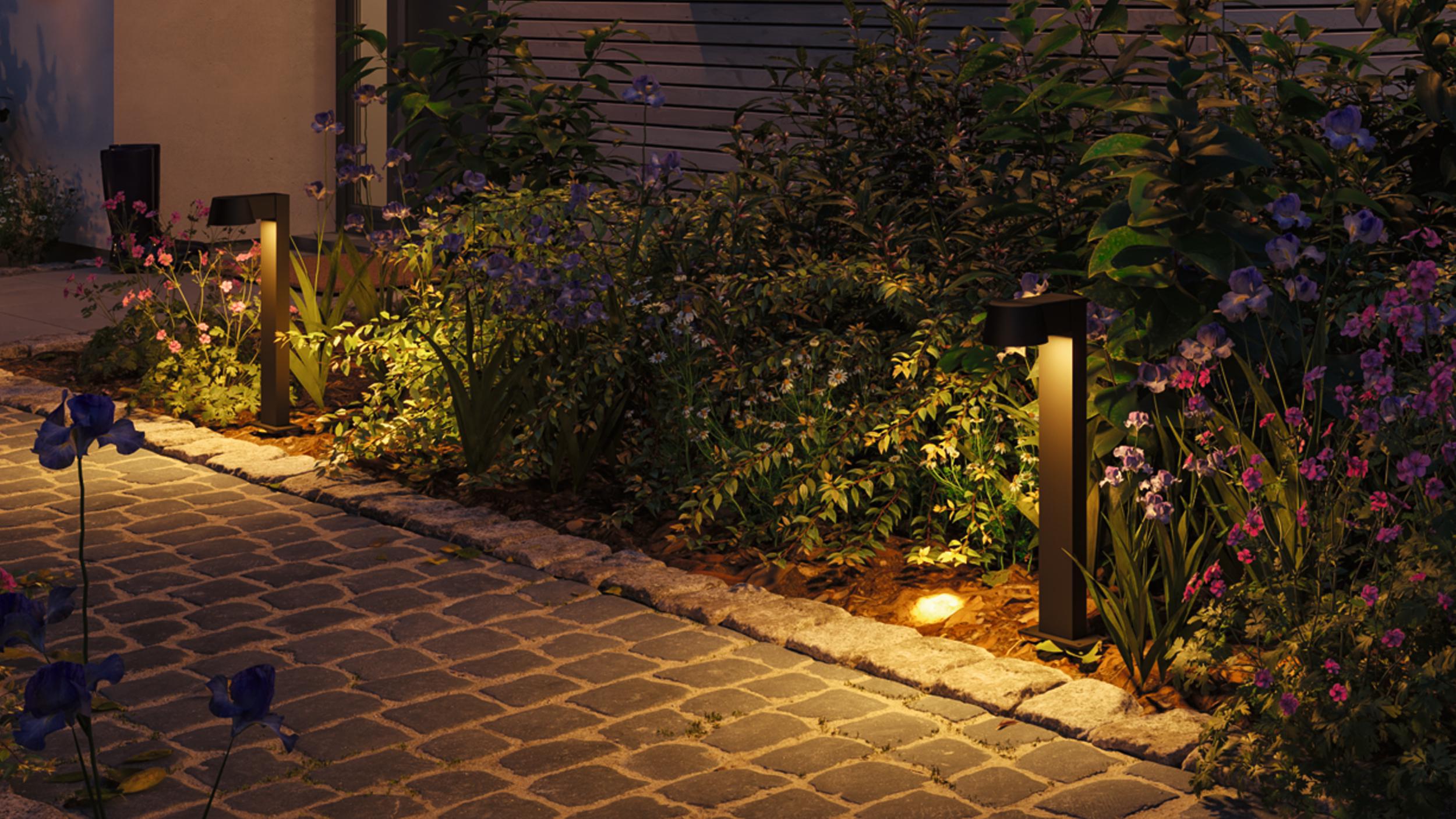 Moderne zwarte tuinlampen met warm wit licht verlichten milieuvriendelijk bloembed en kasseien.