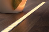 Schlanke LED-Einbauleuchte mit warmweißem Licht auf dunklem Holzfußboden für indirekte Beleuchtung