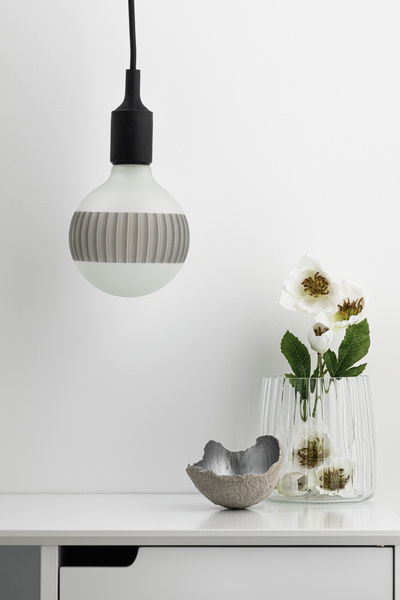 Modern pendant light with frosted white glass bulb and black cable above white sideboard with vase and decor.