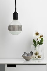 Suspension moderne avec ampoule en verre blanc givré et câble noir au-dessus d'un buffet blanc avec vase et déco.