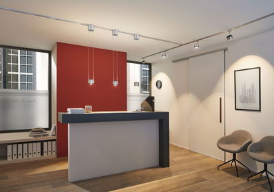 Moderne receptieruimte met zwart-witte balie, rode muuraccenten en verstelbare plafondverlichting.