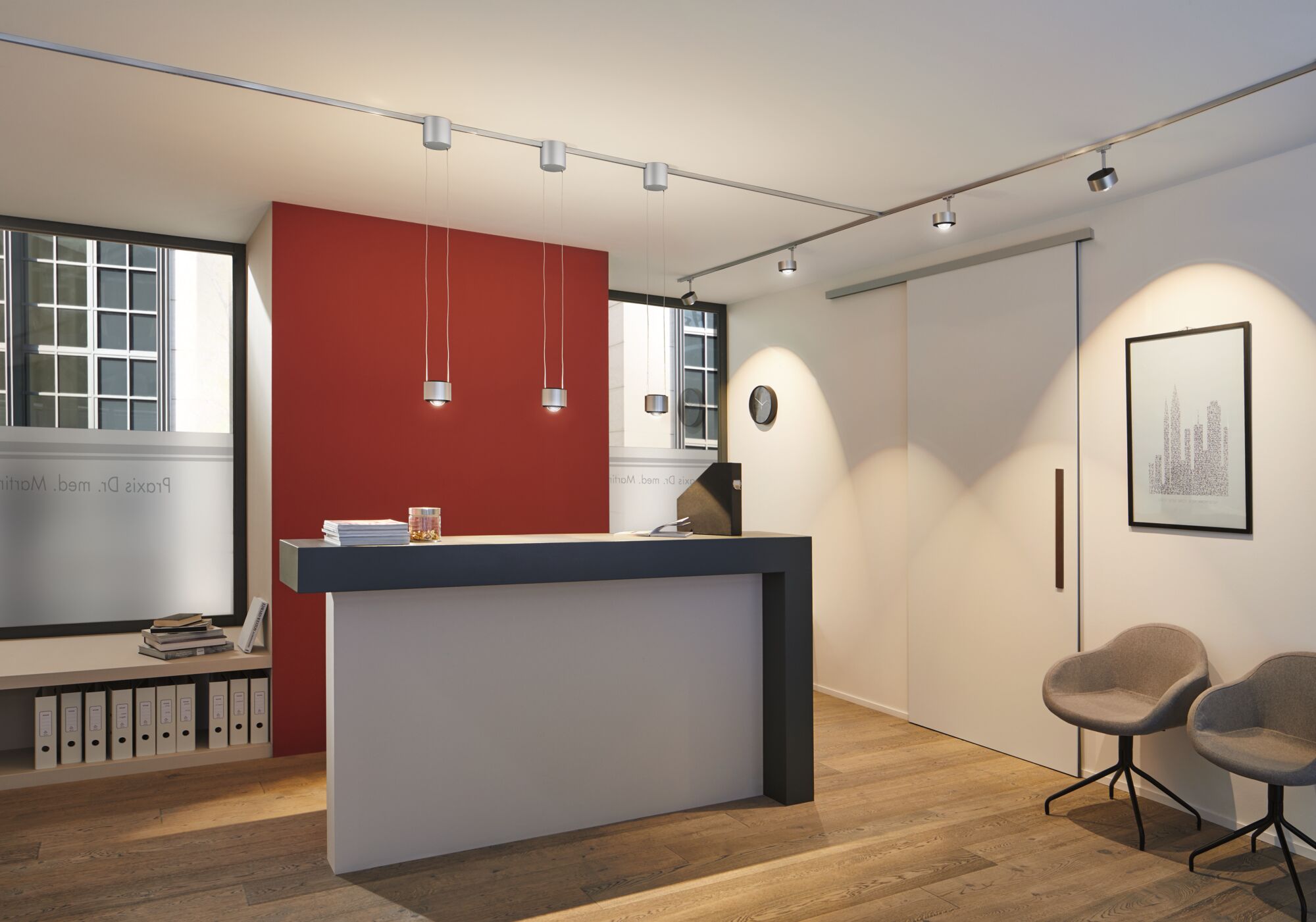 Espace d'accueil moderne avec comptoir noir et blanc, accents muraux rouges et éclairage de plafond réglable.