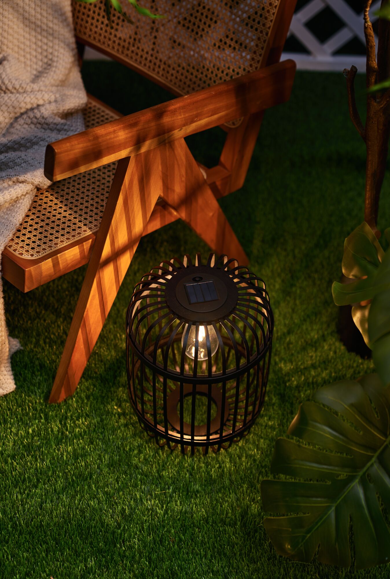 Black metal solar garden lantern with warm white light beside wooden chair on green grass
