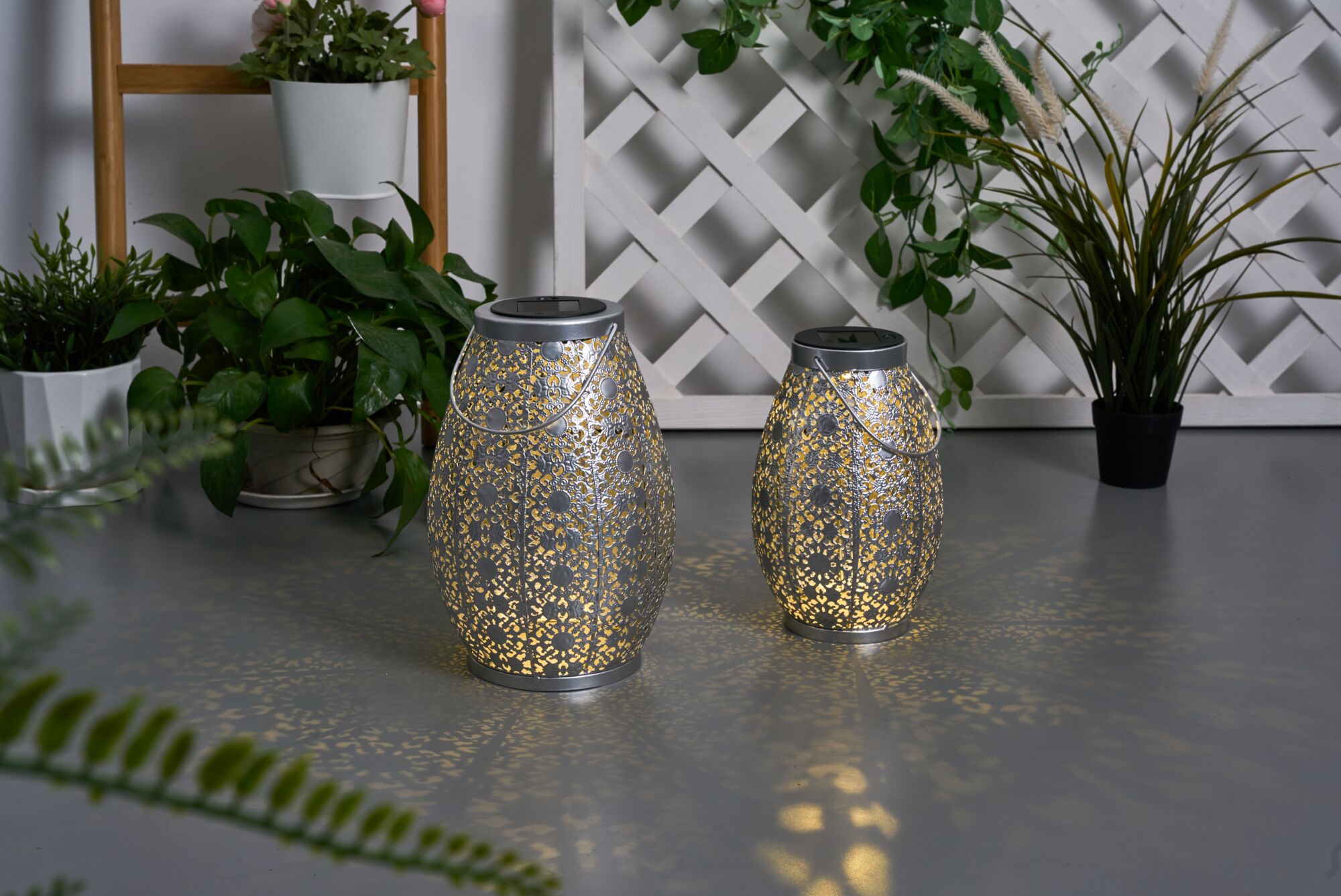 Two silver metal solar lanterns with intricate patterns casting warm light for garden decor.