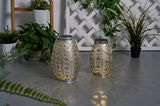 Two silver metal solar lanterns with intricate patterns casting warm light for garden decor.