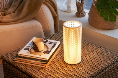 White ceramic table lamp with geometric perforated pattern on woven table in cozy living room