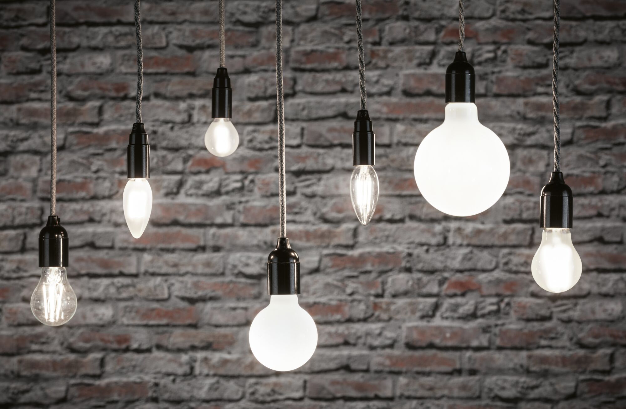 Various filament light bulbs with black sockets hanging in front of a grey brick wall, lighting decor.