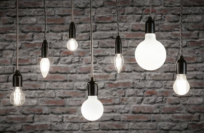 Various filament light bulbs with black sockets hanging in front of a grey brick wall, lighting decor.